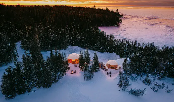 Aerial view of a snowy lakeside landscape in Ontario, with two cabins surrounded by trees.