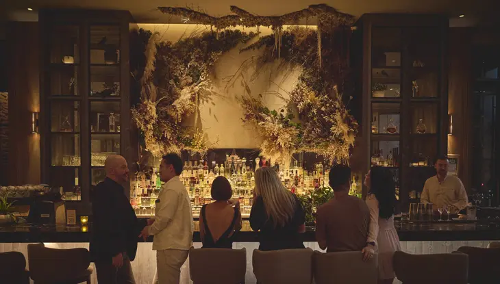 Six patrons stand and sit facing a dramatic bar in the stylish, low-lit lounge at 1 Hotel in Toronto.