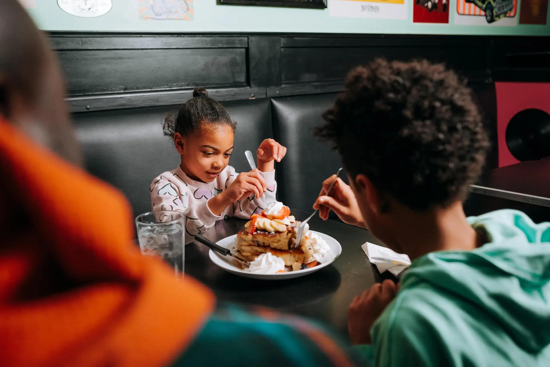 Dos niños pequeños comparten un plato de panqueques apilados cubiertos con fruta y crema batida.