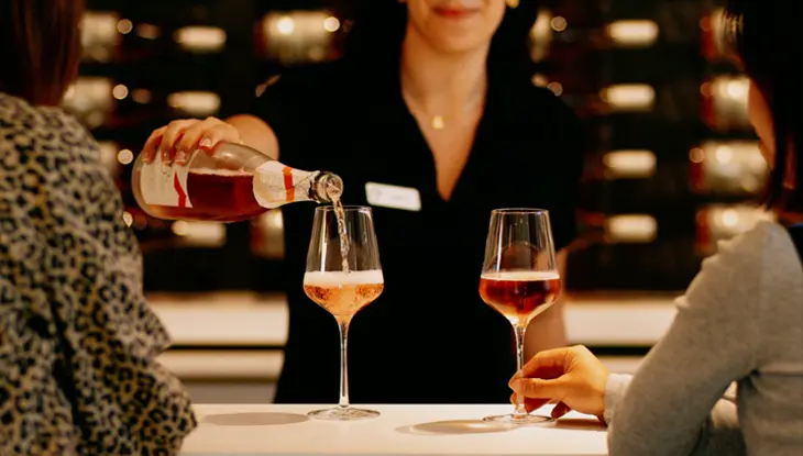 Two women sit at a tasting bar at 13th Street Winery, as a server pours rosé into one of their wineglasses.