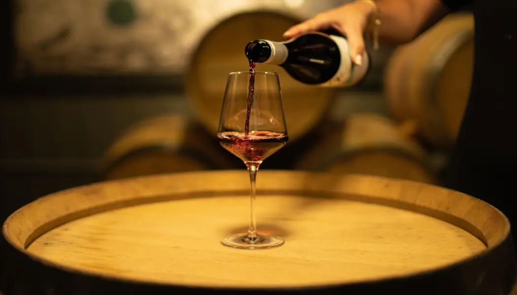 Red wine is poured into a wine glass on a wine barrel table for a tasting at 13th Street Winery.