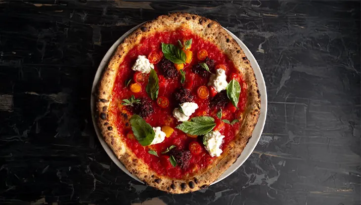 An overhead view of a margarita pizza with red sauce, fresh tomatoes, cheese and basil.