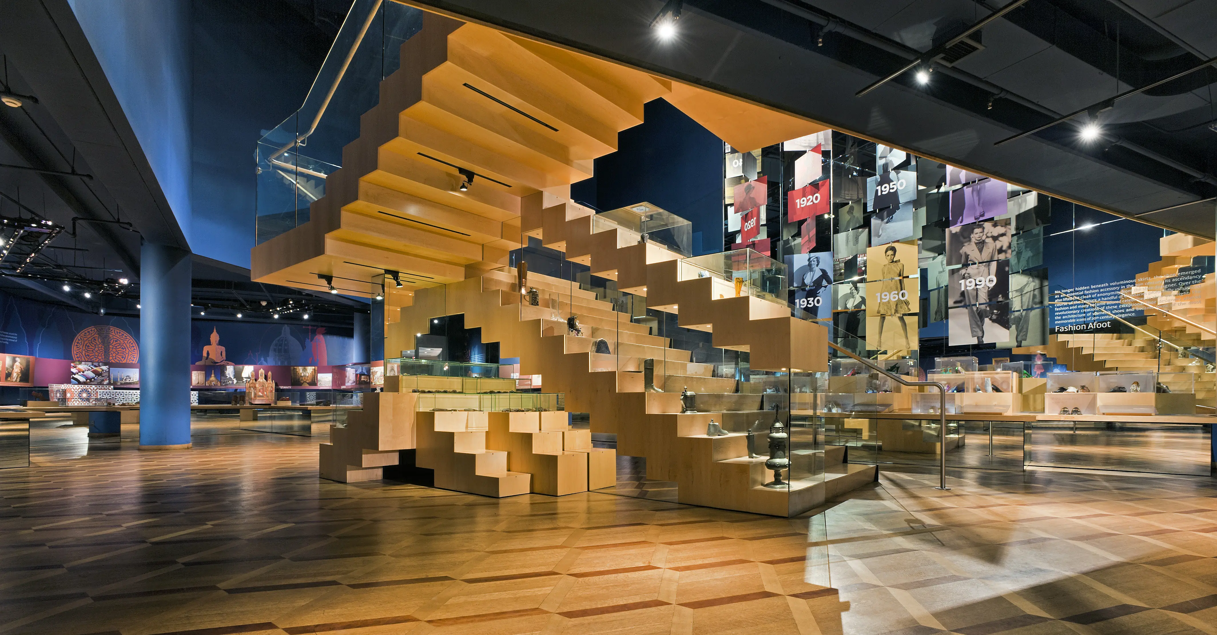 Salle d’exposition du Musée Bata de la chaussure, à Toronto, avec un escalier moderne en bois et des présentoirs d’articles de mode.