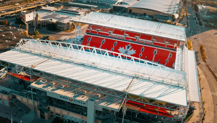 Vue aérienne d'un grand stade entouré de bâtiments urbains au coucher du soleil.