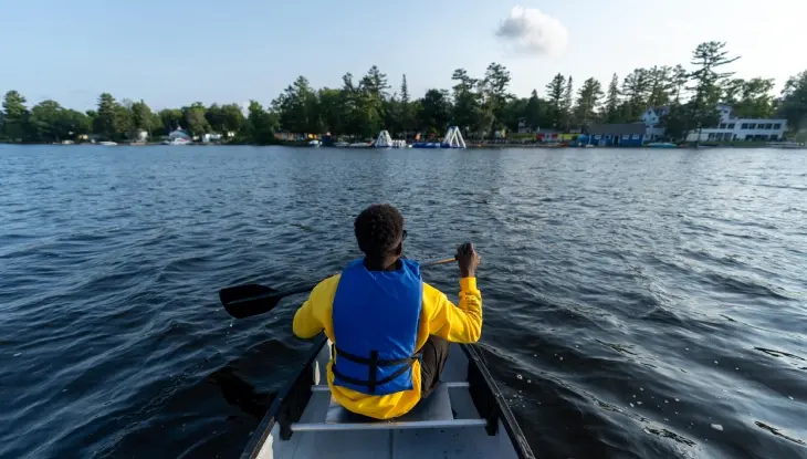 Un jeune garçon portant un gilet de sauvetage pagaye en canoë vers un complexe hôtelier familial situé au bord d'un lac.