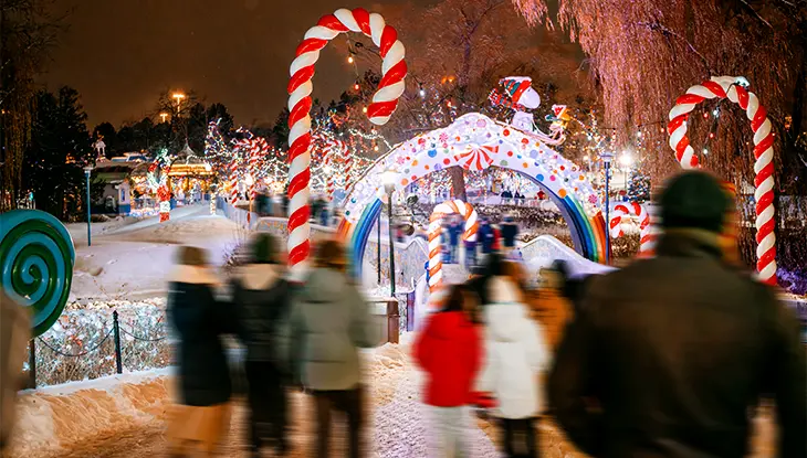 Families walking through a colourful Christmas light display with oversized candy canes at night.