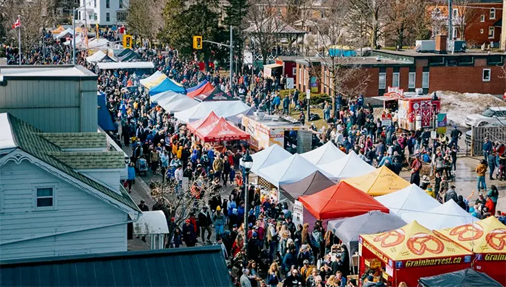 Crowds filling a main street lined with vendor tents during a street festival.