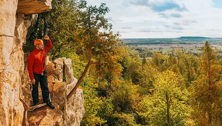 A person raising their hand to block the sunlight standing on the side of a cliff admiring the forest view.