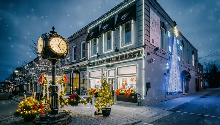 Historic building glowing with colourful festive lights beside a vintage street clock at night.