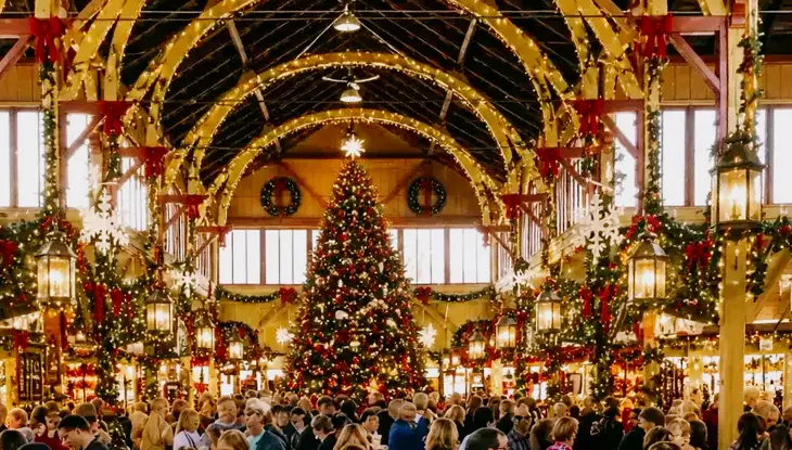 Crowded indoor Christmas market inside a historic hall decorated with festive garlands and warm lights.