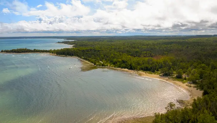 Vista aérea de una playa de arena y aguas tranquilas de color azul verdoso rodeadas de bosque.
