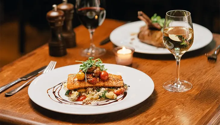Ein Teller mit Gourmet-Lachs und Gemüse auf einem Holztisch, dazu Wein und Kerzenlicht.