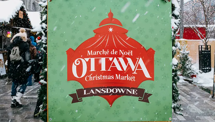 Sign for the Ottawa Christmas Market at Lansdowne surrounded by snow and festive decorations.