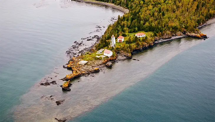Vue aérienne d’une zone côtière où l’on aperçoit des bâtiments blancs aux toits rouges ainsi qu’un grand phare.