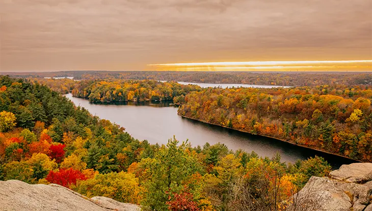 River winding through colourful autumn forest viewed from a rocky lookout under cloudy skies.