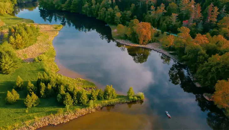 Vista aérea de un río serpenteante rodeado de bosques y tierras de cultivo en otoño, con árboles que muestran vibrantes tonalidades de naranja, amarillo y verde.