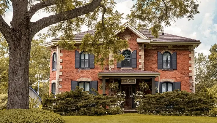 Casa histórica de ladrillo rojo rodeada de árboles maduros y jardines paisajísticos.
