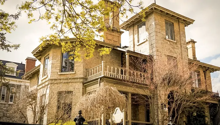 Maison historique en pierre avec des détails architecturaux ornés, des balcons et des arbres environnants.