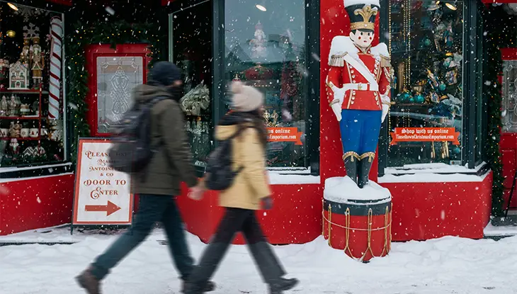Christmas shop window decorated with festive greenery and a nutcracker figure as pedestrians walk by.