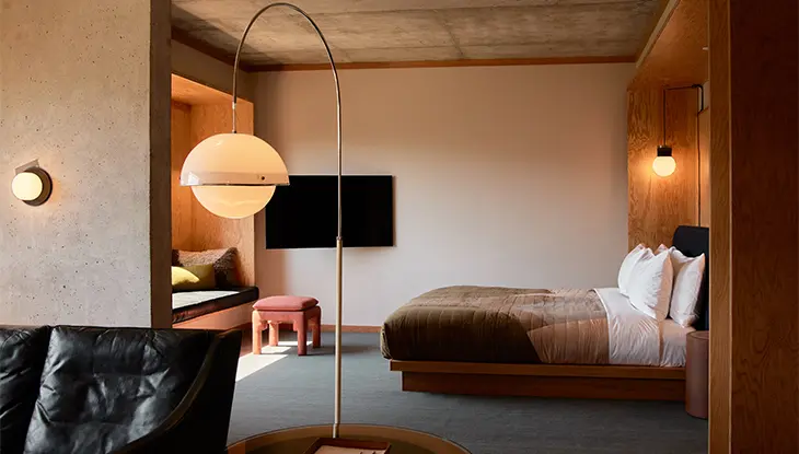 Intérieur moderne d’une suite au Ace Hotel Toronto avec un lit à plateforme, un coin salon et des détails chaleureux en bois.