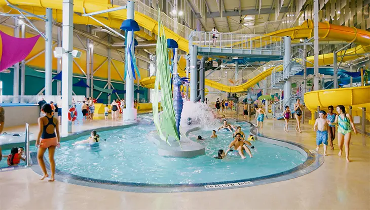 Familles et enfants s’amusant dans un grand parc aquatique intérieur avec glissades et piscines peu profondes.