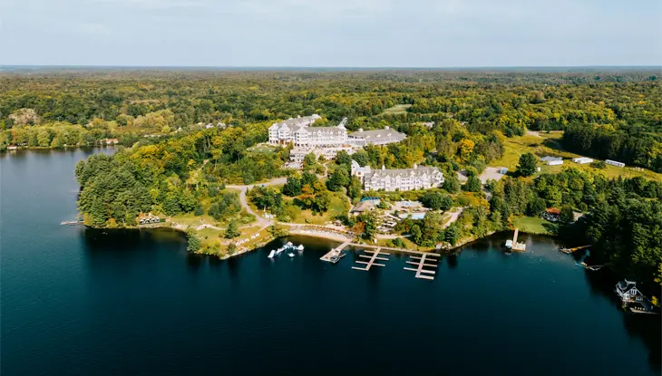 Aerial view of The JW Marriot Rosseau Muskoka Resort & Spa in Minett, Ontario, surrounded by lush greenery, with docks extending into the calm water.