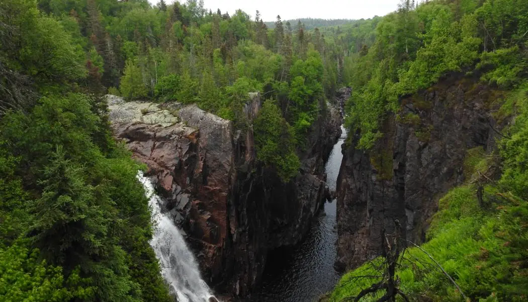 A waterfall cascades down a steep rock face into a narrow river at the bottom of the gorge.