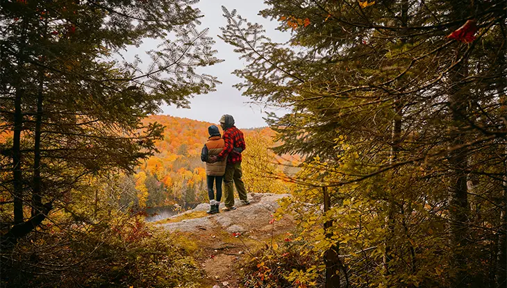 Two hikers standing on a rocky lookout surrounded by fall colours.
