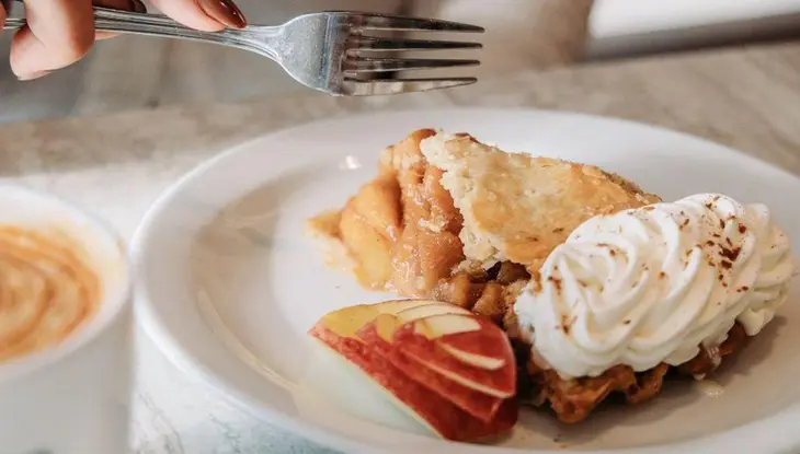 Thornbury Café에서 사과파이, 휘핑크림, 신선한 사과를 자르려고 하는 포크.