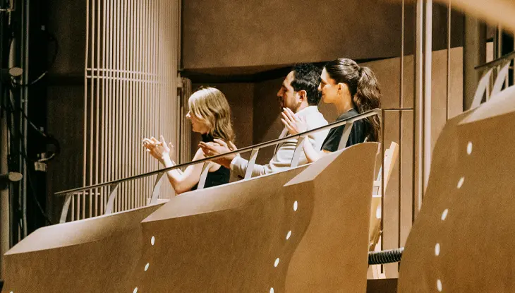 Miembros de la audiencia sentados en un balcón del teatro con vistas al escenario.