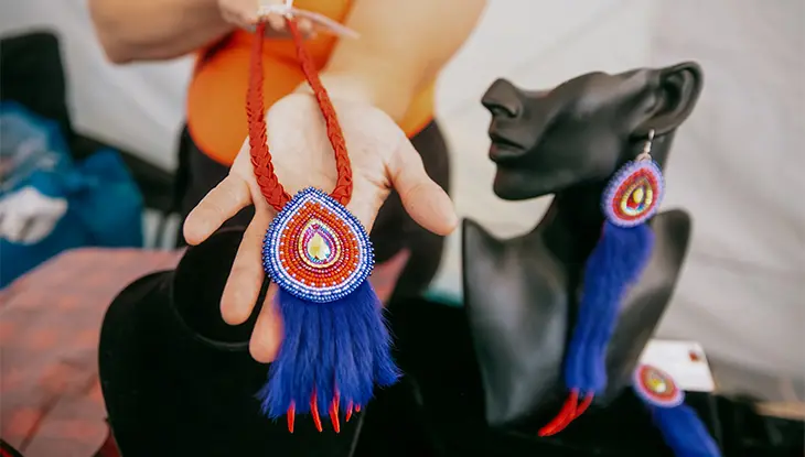 Marchand montrant un magnifique collier de perles aux motifs complexes, avec une boucle d’oreille assortie présentée sur une statue.