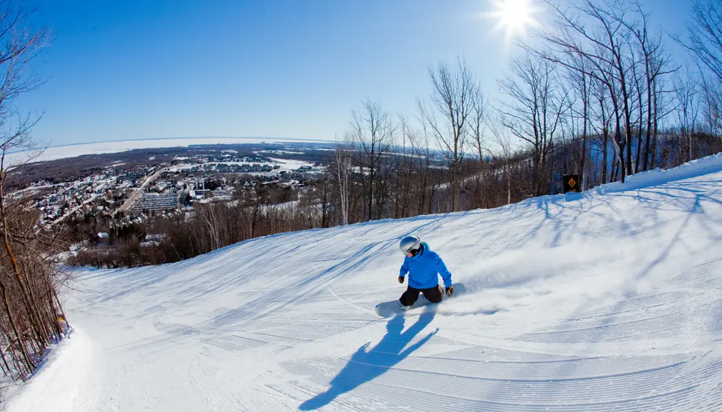 Ein Snowboarder fährt an einem sonnigen Wintertag im Blue Mountain Resort einen gut gepflegten Schneehang hinunter.