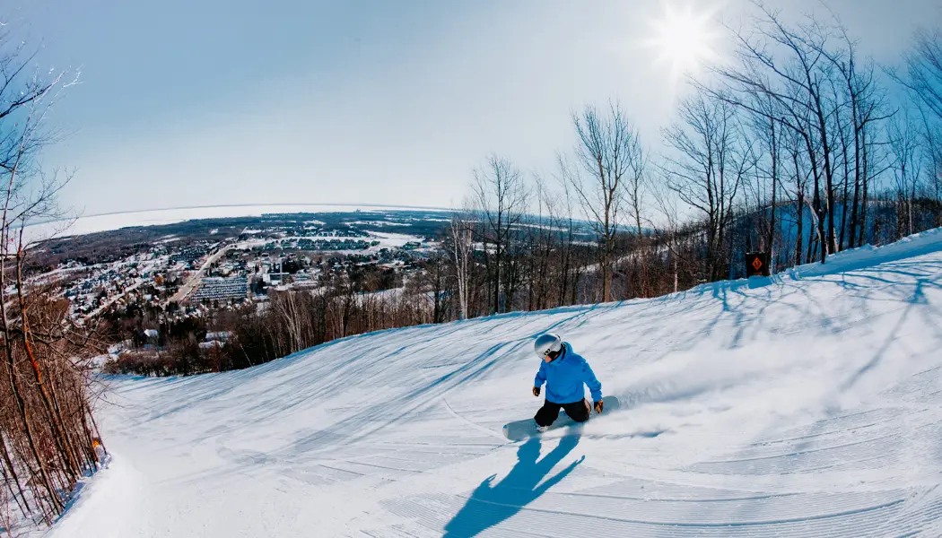 Planchiste dévalant une pente de neige bien entretenue par une journée d’hiver ensoleillée au centre de villégiature Blue Mountain.