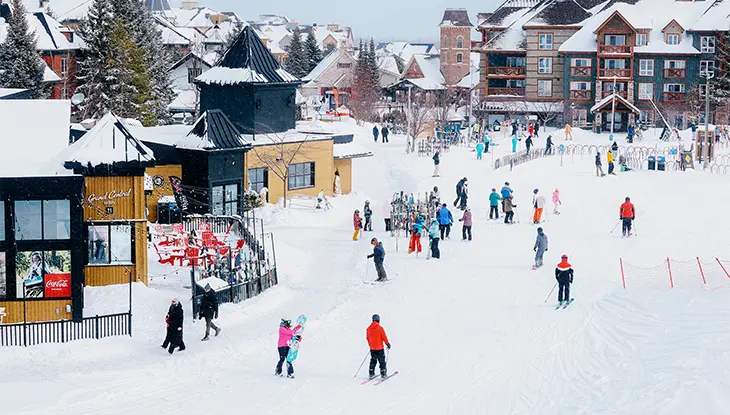 ブルーマウンテンの雪に覆われたスキー村。スキーヤーや観光客がショップ、レストラン、シャレー風の建物の間を歩いています。