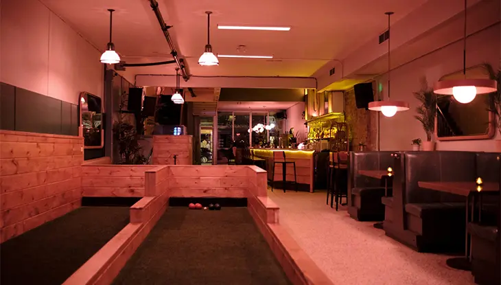 Elegante salón de bolos interior con pistas de madera, zonas de estar y una cálida iluminación ambiental.