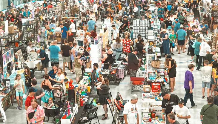 Large crowd browsing vendor booths at an indoor comic and pop culture event.