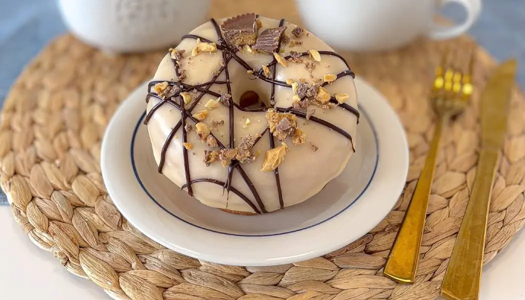 Un beignet artisanal décoré avec art et nappé de chocolat, servi sur une assiette avec des couverts en or.