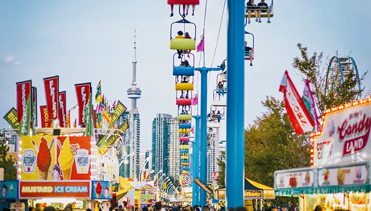 Foule au travers des manèges et stands de restauration à l’Exposition nationale canadienne, avec la Tour CN en arrière-plan
