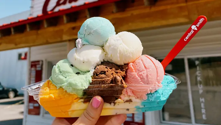 Close up of a bowl with several scoops of ice cream in front of Central Smith Creamery.