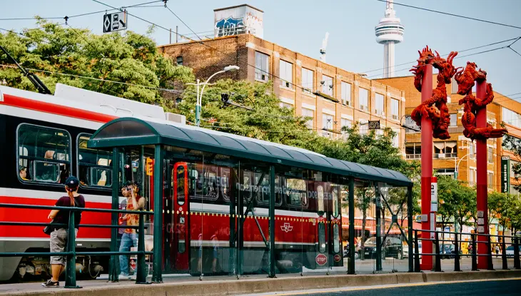 Un tramway rouge était arrêté en plein jour dans une rue de la ville, avec de grandes sculptures de dragons rouges et des bâtiments en briques en arrière-plan.