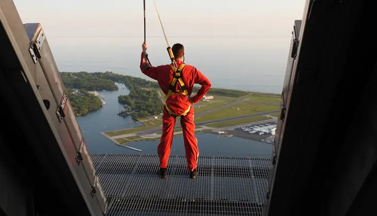 Un homme portant une combinaison rouge et un équipement de sécurité se tient sur la plate-forme extérieure d'EdgeWalk à la Tour CN.