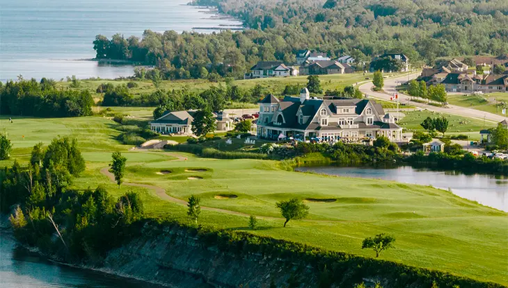 Luftaufnahme eines Golfplatzes und Clubhauses mit Blick auf ein großes Gewässer.