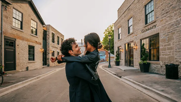A couple hugging and smiling at each other on a cobblestone street in Elora.
