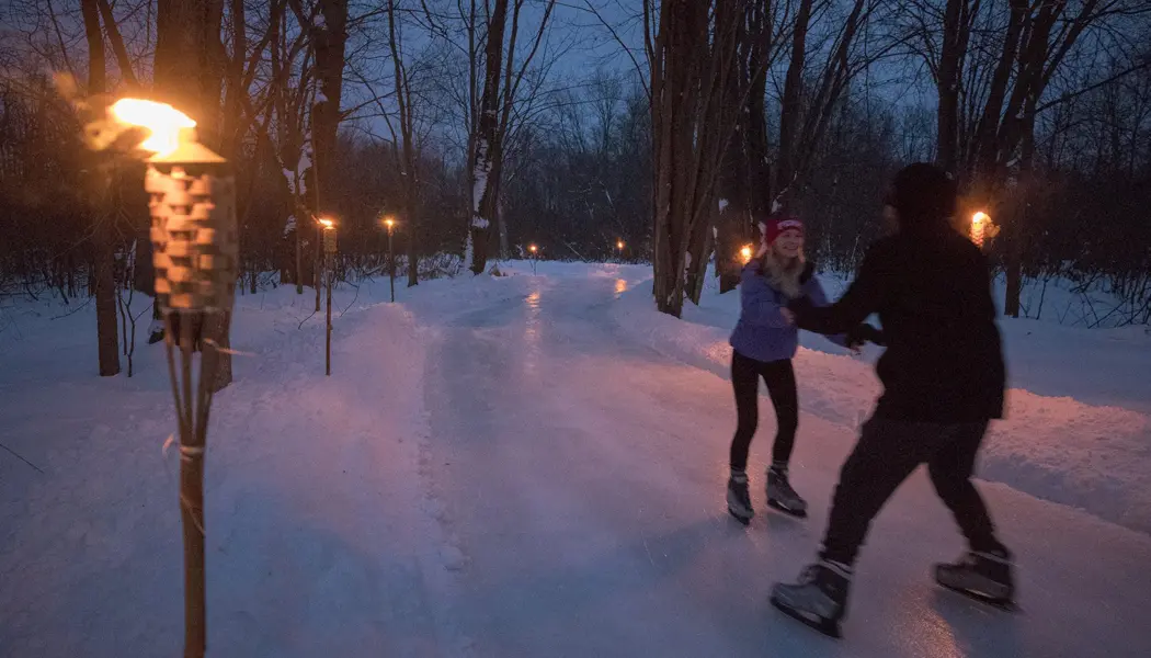 Couple patinant de nuit le long du sentier de patinage du centre de villégiature Fern à la lumière des torches tiki