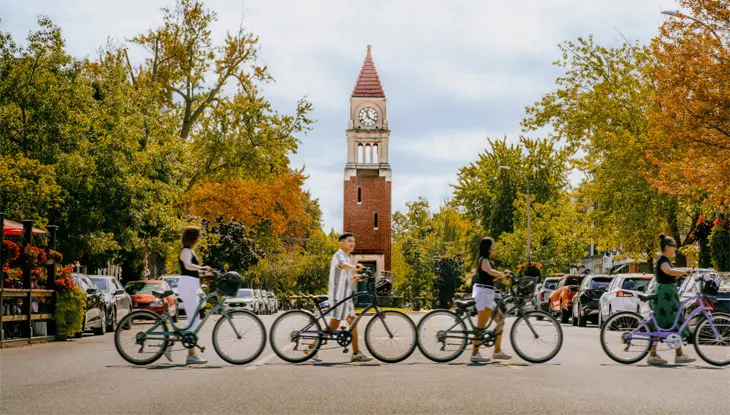 Four people walk bicycles across the main street in downtown Niagara-on-the-Lake.