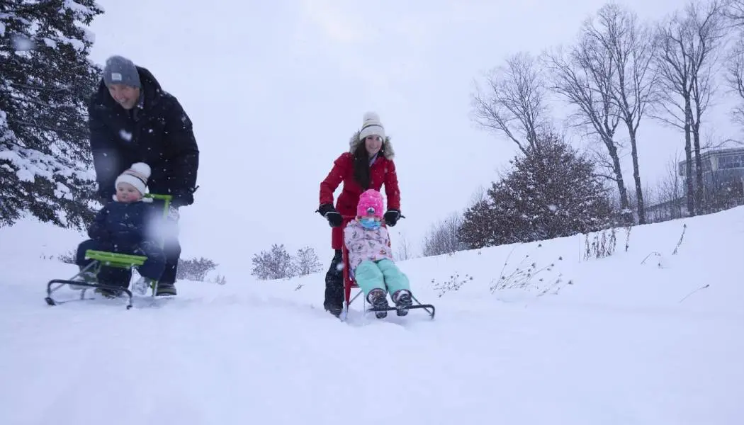 Des parents poussent deux jeunes enfants sur des luges en bas d'une colline enneigée dans une station de sports d'hiver familiale de l'Ontario.