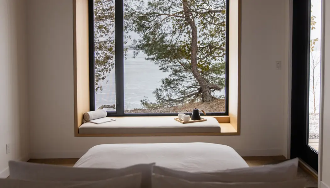 小屋の寝室の窓から見える松の木と湖の静かな景色。