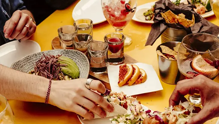 People sitting at a table grabbing various types of Mexican cuisine.