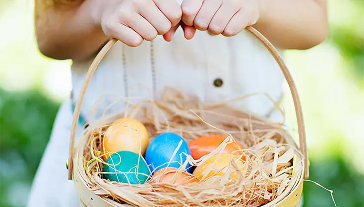 Enfant tenant un panier rempli d’œufs de Pâques colorés à l’Easter Eggstravaganza au domaine Puddicombe.