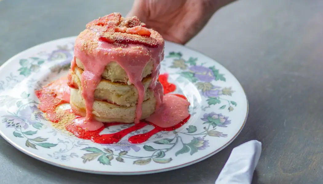 Three juicy waffles layered with strawberry cheesecake sauce are served on a floral plate for brunch.